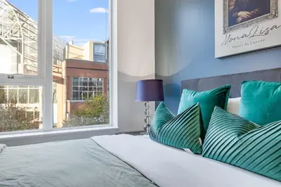 a bedroom with a bed with green pillows and a window at Stylish 2BR Downtown Condo By Arena Free Parking in Vancouver