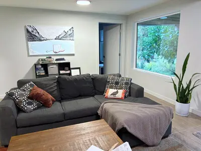 a living room with a gray couch and a window at Coastal Drift Sooke in Sooke