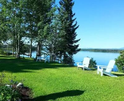 two white benches sitting on the grass near the water at Retreat Wilderness Inn in Nimpo Lake