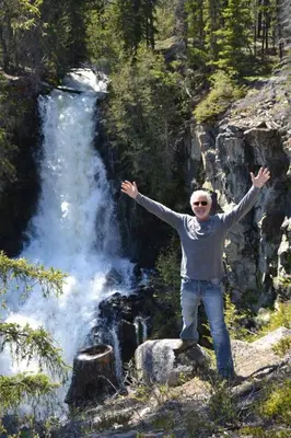 a man standing on a rock in front of a waterfall at Retreat Wilderness Inn in Nimpo Lake