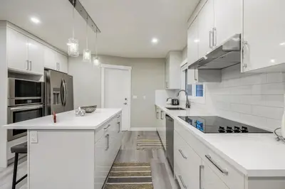 a white kitchen with white cabinets and appliances at Renovated 3BE, 2BA close to UoC, downtown, SAIT in Calgary