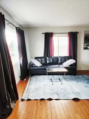 a living room with a black leather couch and a blue rug at House in Edmonton