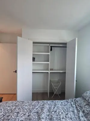 a bedroom with a bed and white walls and shelves at Comfortable Home Near Hospitals and Parks in Calgary