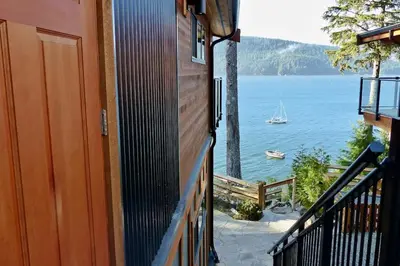 a balcony with a view of a boat in the water at Wickham's Wake - 3BR Oceanfront - pet friendly in Port Renfrew