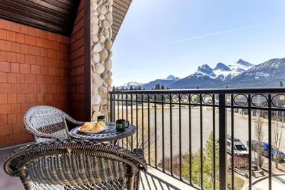 a table and a chair on a balcony with mountains at Stunning Penthouse with Mtn Views Hot Tub and Pool in Canmore