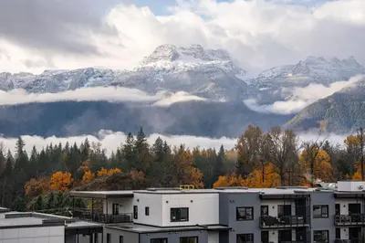a view of a snowy mountain with clouds and buildings at The Ridge - 3 Bedroom Condo - Roof Top Hot Tub in Revelstoke