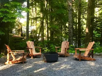 three wooden chairs and a fire pit in a forest at Private treed setting - no pets - garden view in Port Renfrew