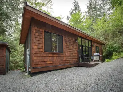a cabin in the woods with a large window at Private treed setting - no pets - garden view in Port Renfrew