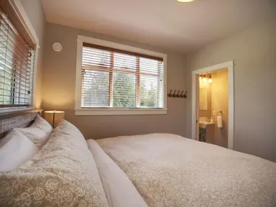 a bedroom with a large bed and two windows at Oceanfront & Amazing Views - Pet Friendly - 2bdrm in Port Renfrew