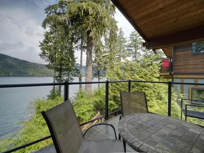 a patio with a table and chairs and a view of a lake at Hera's Cove - Oceanfront Oasis - Pet Friendly in Port Renfrew