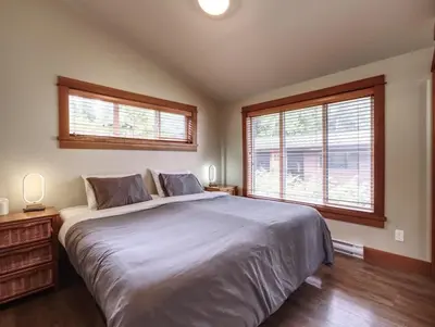 a bedroom with a large bed and two windows at Going Coastal A - Oceanfront - Pet Friendly in Port Renfrew