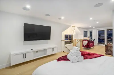 a white bedroom with a flat screen tv on the wall at Trendy Bridgeland, Fireplace, King Beds, AC in Calgary