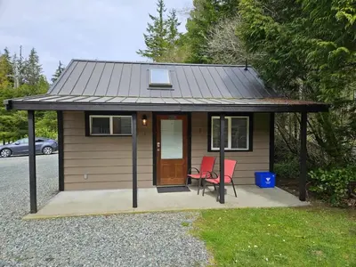a small cabin with two red chairs in front of it at Cozy Rainforest Cottage for 2 - Pet Friendly in Port Renfrew