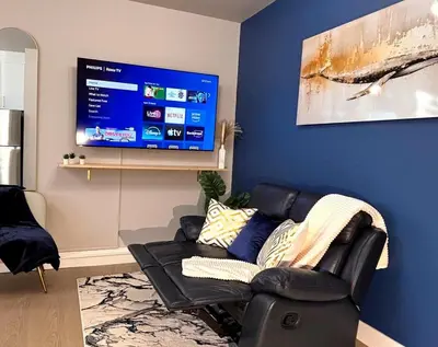 a living room with a black leather couch and a flat screen tv at Ocean-Inspired Art Suite in Langford