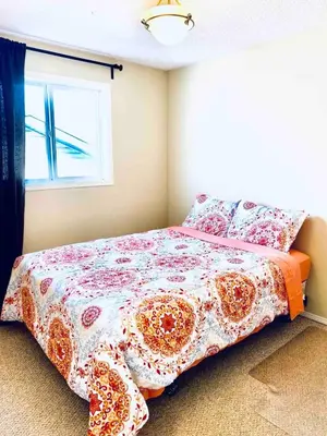 a bedroom with a bed with a flowered blanket and a window at Spacious 3BR Retreat w-Hot Tub Ravine Sleeps 9 in Edmonton