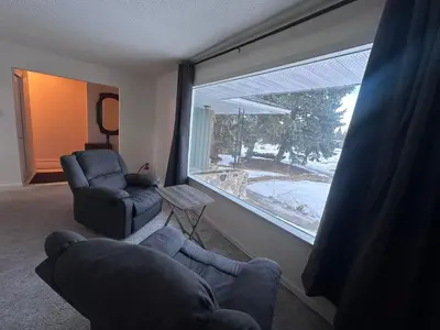 a living room with a couch and a chair and a large window at 3 Private rooms with built-in closet & desk in Edmonton