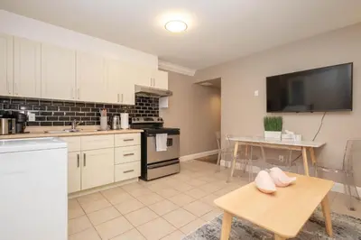 a kitchen with white cabinets and a table and a tv at Modern 2BR Suite | 10 Mins to YVR & Canada Line in Vancouver