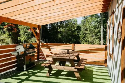 a wooden patio with a picnic table and a grill at Quadra Island Mist in Quathiaski Cove