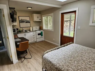 a bedroom with a bed and a desk and a kitchen at Rustic Rainforest Cabin for 2 - Peaceful - Pet Friendly in Port Renfrew