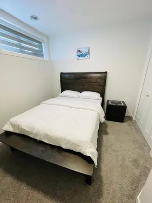 a bedroom with a bed with white sheets and a window at Modern Comfort in NW Calgary in Calgary