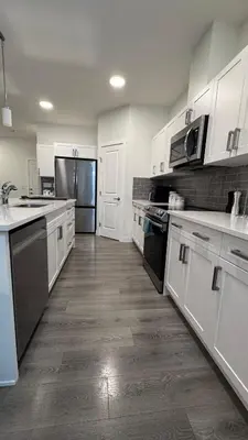 a kitchen with white cabinets and a wooden floor at Heartland Stays - Brand New 3 Bed Room Cozy Home in Cochrane