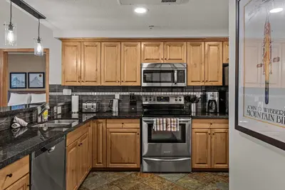 a kitchen with wooden cabinets and stainless steel appliances at Tranquil Condo In The Trees Spacious 2Bd Hot Tub & Pool in Canmore