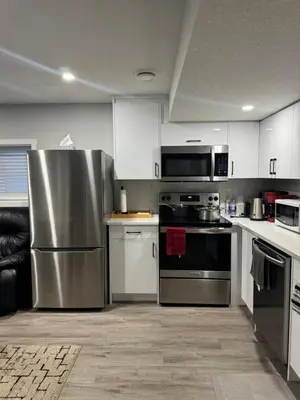 a kitchen with stainless steel appliances and white cabinets at Cozy 2 Bedroom Basement Apartment in Calgary