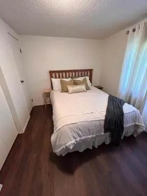 a bedroom with a bed with white sheets and wooden floors at Cozy Country Cabin in Lacombe