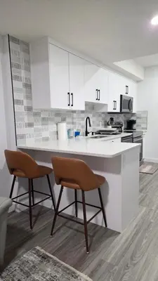 a white kitchen with white cabinets and two chairs at 2BR 14minsYYC Airport Private Entrance Soft Water System in Calgary