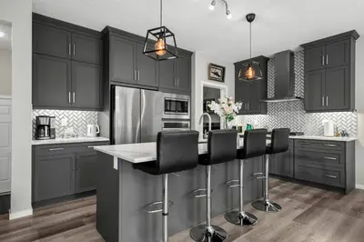 a kitchen with black cabinets and a kitchen island with black chairs at Bright & Spacious Family Retreat in Calgary
