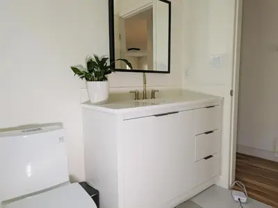 a white bathroom with a sink and a mirror at Private room in Chic Main St suite in Vancouver