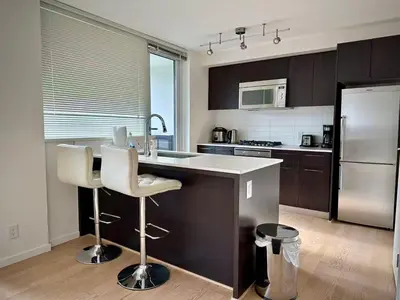 a kitchen with a counter with two chairs and a refrigerator at Pleasant and convenient 1B1B close to Richmond Center in Richmond