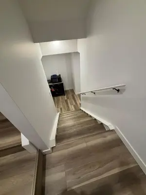 a staircase with white walls and wooden floors at Fowler Road Cozy Lower Suite in Airdrie