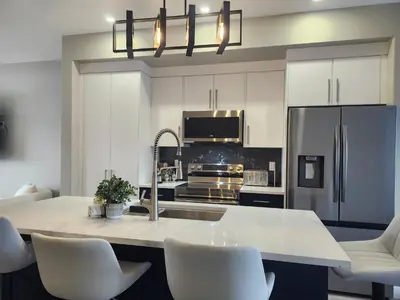 a kitchen with white cabinets and a kitchen island with white chairs at Harmony Haven in Drumheller in Drumheller