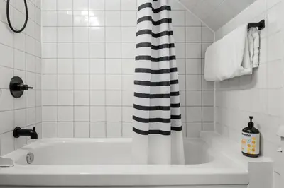 a white bathroom with a tub and a black and white shower curtain at Mid Century Zen Suite. 1 BR. Near DT, C-train. in Calgary