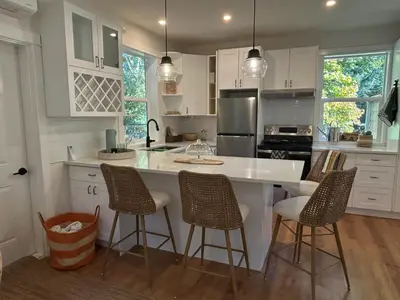 a kitchen with white cabinets and a island with bar stools at Retreat to Quail Cottage in Chemainus