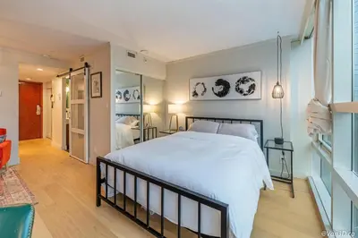 a bedroom with a large white bed and a hallway at Beautiful Downtown Studio with Parking in Vancouver