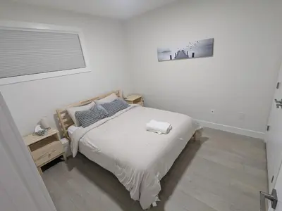 a white bedroom with a bed and a window at Greystone Retreat - Walk to River & Downtown in Cochrane