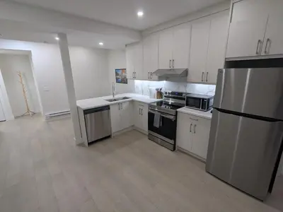a kitchen with white cabinets and a stainless steel refrigerator at Greystone Retreat - Walk to River & Downtown in Cochrane