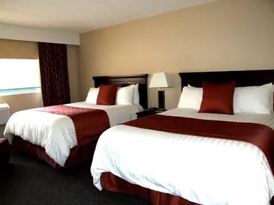 two beds in a hotel room with white and red at Lakeland Inn Hotel in Cold Lake