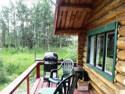 a porch of a log cabin with chairs and a grill at Nimpo Lake Resort in Nimpo Lake