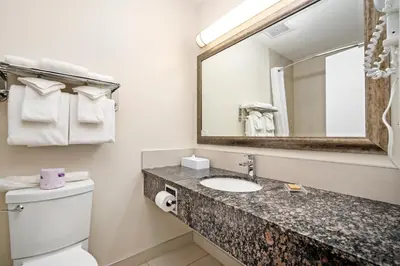 a bathroom with a toilet and a sink and a mirror at Guest House Inn & Suites in Edson