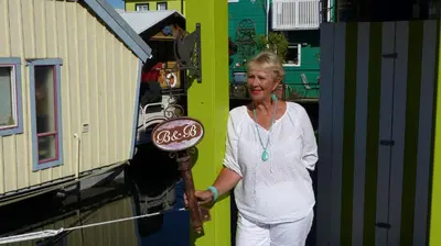 a woman standing next to a building with a sign at A Float Home B&B in Fisherman’s Wharf in Victoria