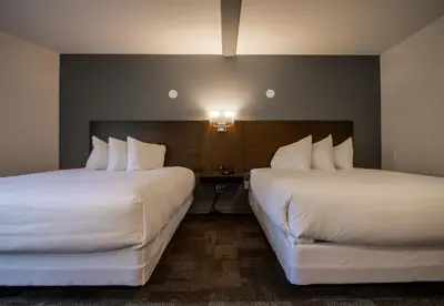 two beds in a hotel room with white sheets at Bedrock Motel in Mayo Landing