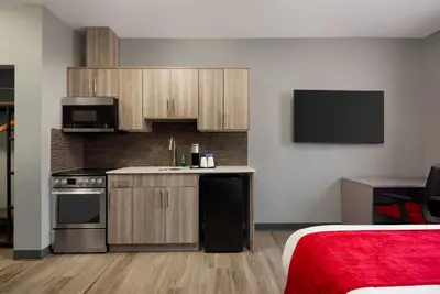 a kitchen with wooden cabinets and a bed in a room at Ramada by Wyndham West Edmonton Hotel & Suites in Edmonton