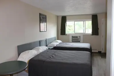 two beds in a room with a table and a window at Plains Motor Inn in Stettler