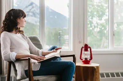 a woman sitting in a chair while holding a book at Elk + Avenue Hotel in Banff