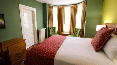 a bedroom with a white bed with green walls and windows at James Bay Inn Hotel, Suites & Cottage in Victoria