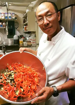 a man holding a pan of carrots in a kitchen at James Bay Inn Hotel, Suites & Cottage in Victoria