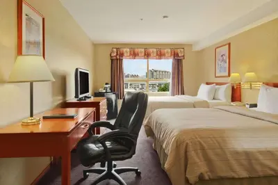 a hotel room with two beds and a desk and a chair at Days Inn by Wyndham Vancouver Airport in Richmond